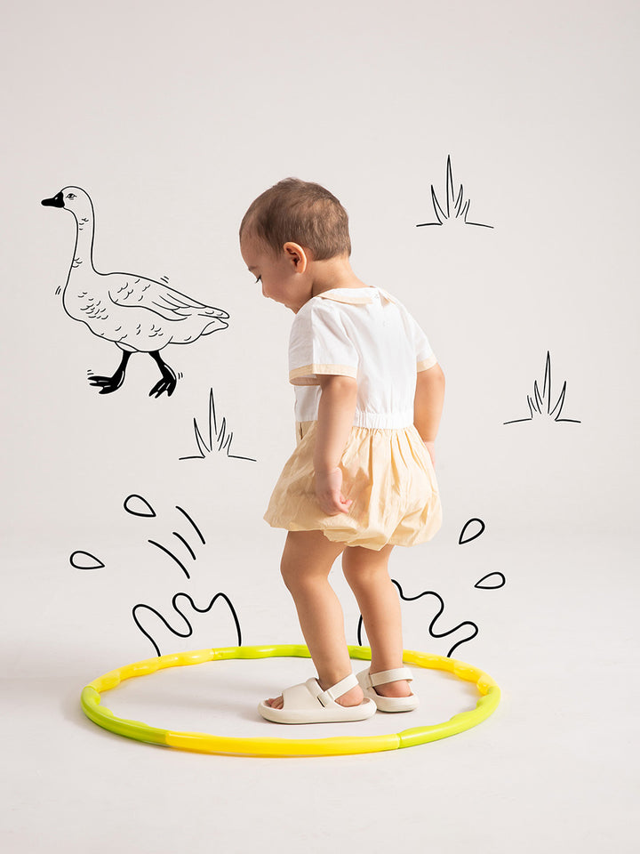 Newborn Baby Beige Organic Cotton One-Piece playing with hula hoop