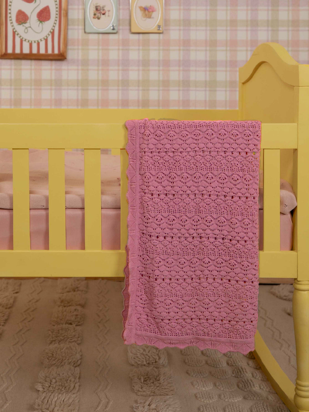 Blush pink cotton knit baby blanket with scalloped edges draped over crib in nursery