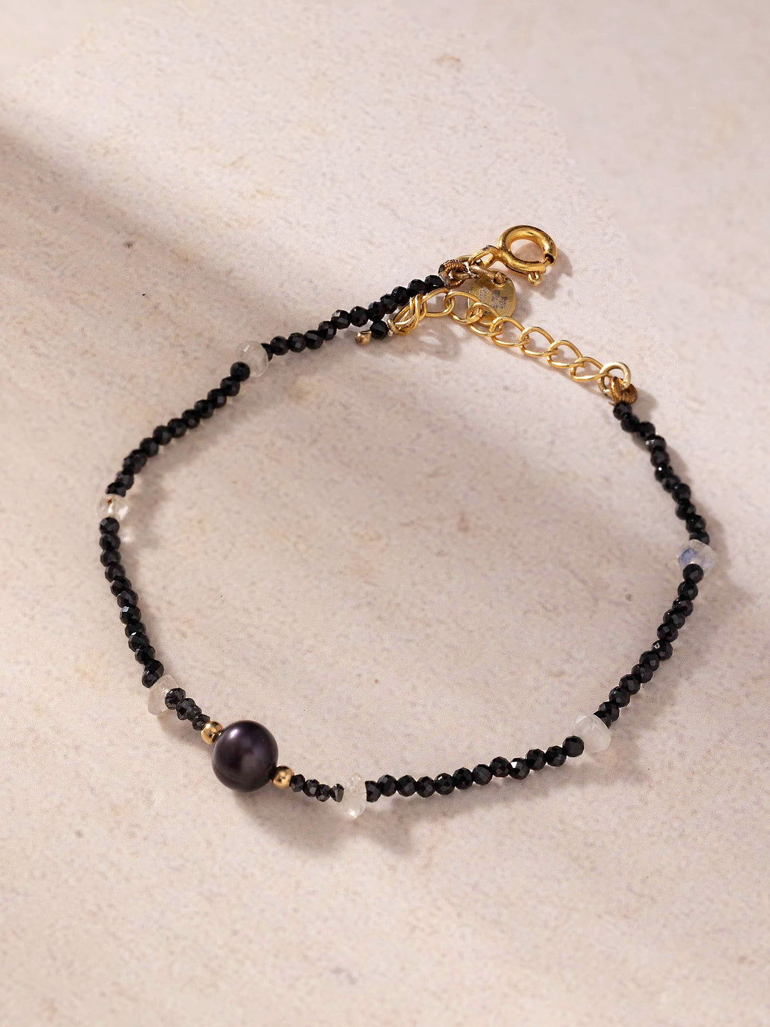 Black beaded bracelet with a gold clasp on a beige surface